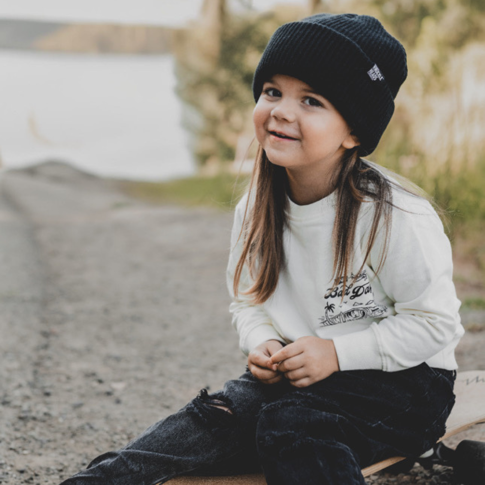 Knuckleheads Off-White Infant Crew Neck for kids, surf-inspired design in lightweight, breathable 100% cotton fabric, displayed against a laid-back, coastal-themed background. Available in sizes from 12 months to 8 years, this top is perfect for casual playdates, beach days, or park outings. Shown with durable, easy-to-wash fabric for stylish, everyday comfort.