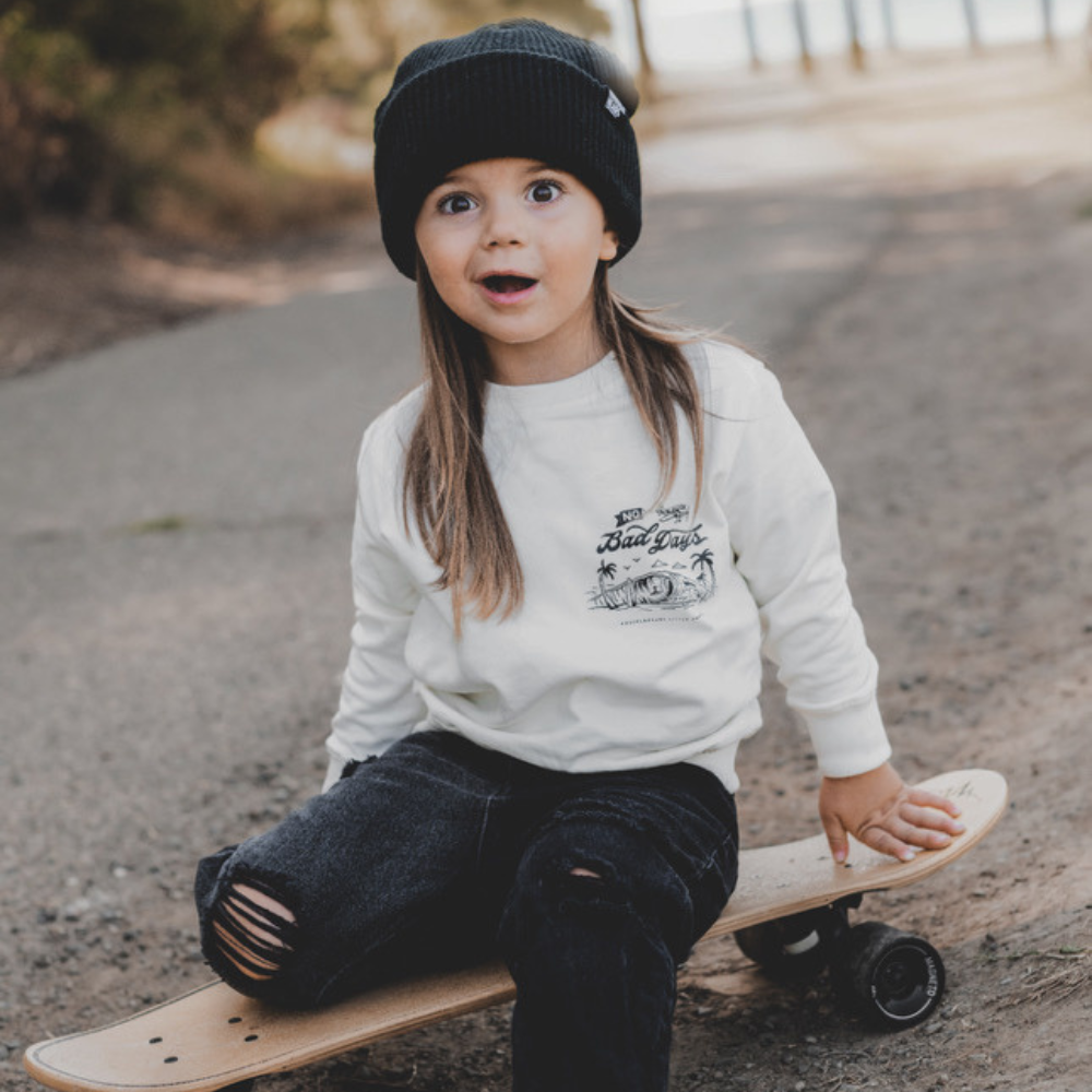 Knuckleheads Off-White Infant Crew Neck for kids, surf-inspired design in lightweight, breathable 100% cotton fabric, displayed against a laid-back, coastal-themed background. Available in sizes from 12 months to 8 years, this top is perfect for casual playdates, beach days, or park outings. Shown with durable, easy-to-wash fabric for stylish, everyday comfort.