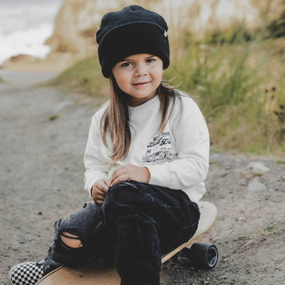 Knuckleheads Off-White Infant Crew Neck for kids, surf-inspired design in lightweight, breathable 100% cotton fabric, displayed against a laid-back, coastal-themed background. Available in sizes from 12 months to 8 years, this top is perfect for casual playdates, beach days, or park outings. Shown with durable, easy-to-wash fabric for stylish, everyday comfort.