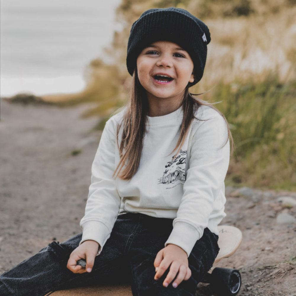 Knuckleheads Off-White Infant Crew Neck for kids, surf-inspired design in lightweight, breathable 100% cotton fabric, displayed against a laid-back, coastal-themed background. Available in sizes from 12 months to 8 years, this top is perfect for casual playdates, beach days, or park outings. Shown with durable, easy-to-wash fabric for stylish, everyday comfort.