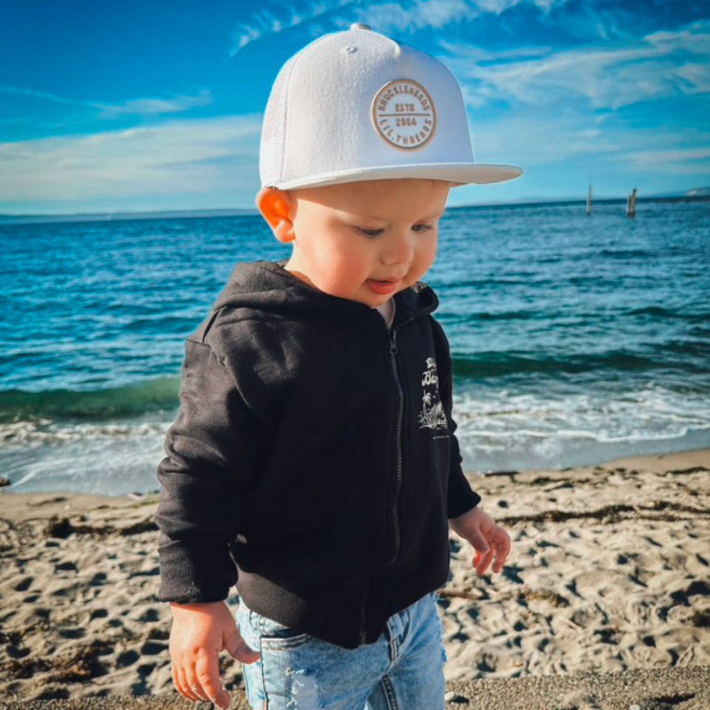 Hawaii Off White Snapback hat for infants and toddlers, crafted from 100% cotton for soft, comfortable wear. Features a medium-profile, structured 5-panel crown with a flat bill and adjustable snapback closure for a perfect fit as they grow. Embroidered tan Knuckleheads patch adds a stylish touch, ideal for little adventurers