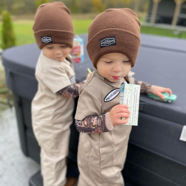 This image showcases delightful camel kids' coveralls adorned with a charming Knuckleheads patch, adding a touch of whimsy to your child's wardrobe. These coveralls are not only fashionable but also comfortable, making them an ideal choice for your little one's everyday adventures.