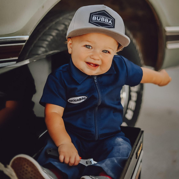 This image showcases delightful navy kids' coveralls adorned with a charming Knuckleheads patch, adding a touch of whimsy to your child's wardrobe. These coveralls are not only fashionable but also comfortable, making them an ideal choice for your little one's everyday adventures.