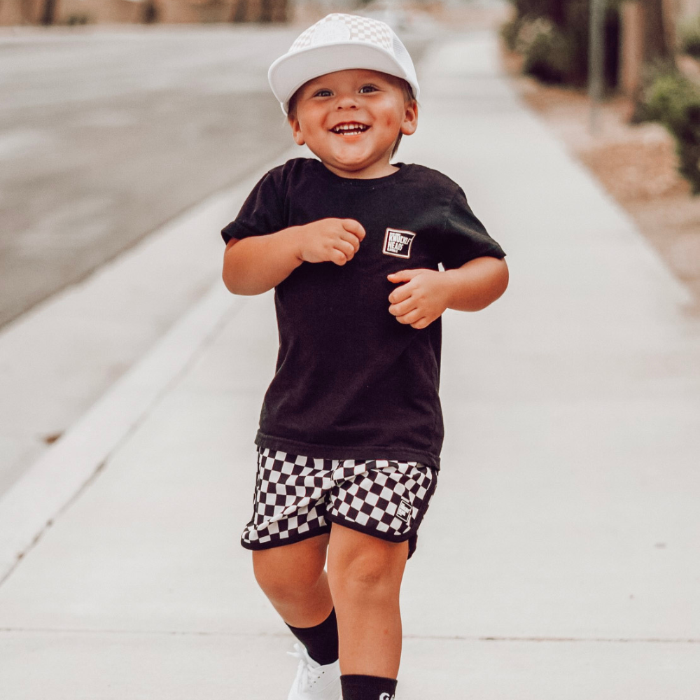 Image of White Kids Trucker Hat with Knuckleheads Patch and Checkered Pattern: A hip and stylish trucker hat designed for kids. The hat comes in crisp white and features a fashionable Knuckleheads patch adorned with a cool checkered pattern. Made with no sun mesh for a comfortable and breathable wear. Perfect accessory to elevate your child's style while providing sun protection.