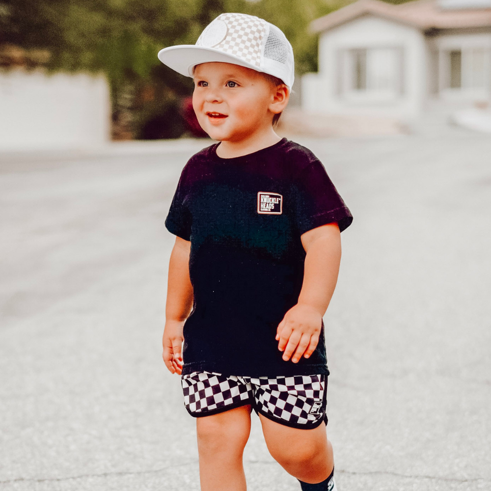 Image of White Kids Trucker Hat with Knuckleheads Patch and Checkered Pattern: A hip and stylish trucker hat designed for kids. The hat comes in crisp white and features a fashionable Knuckleheads patch adorned with a cool checkered pattern. Made with no sun mesh for a comfortable and breathable wear. Perfect accessory to elevate your child's style while providing sun protection.