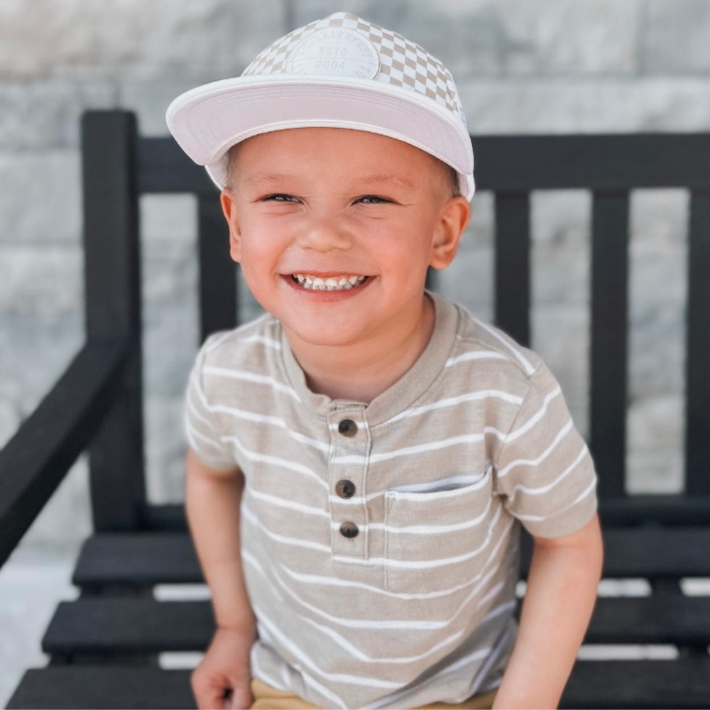 Image of White Kids Trucker Hat with Knuckleheads Patch and Checkered Pattern: A hip and stylish trucker hat designed for kids. The hat comes in crisp white and features a fashionable Knuckleheads patch adorned with a cool checkered pattern. Made with no sun mesh for a comfortable and breathable wear. Perfect accessory to elevate your child's style while providing sun protection.