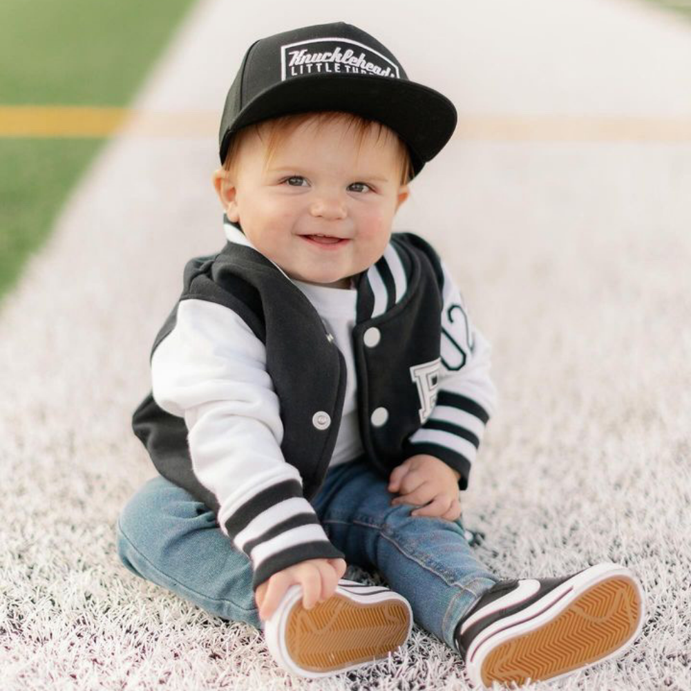 Model wearing a Black Kids Trucker Hat with Knuckleheads Patch. A trendy and versatile accessory designed for kids. In classic black, it showcases a striking Knuckleheads patch on the front. Elevate your child's style with this fashionable hat, perfect for adding a touch of character to their outfits. Crafted with care, this black kids trucker hat with the Knuckleheads patch is a must-have addition to their wardrobe, suitable for various occasions and everyday wear.