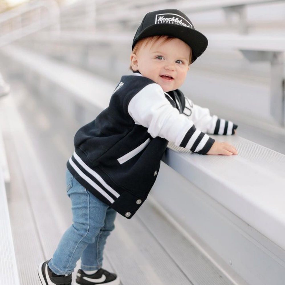 Model wearing a Black Kids Trucker Hat with Knuckleheads Patch. A trendy and versatile accessory designed for kids. In classic black, it showcases a striking Knuckleheads patch on the front. Elevate your child's style with this fashionable hat, perfect for adding a touch of character to their outfits. Crafted with care, this black kids trucker hat with the Knuckleheads patch is a must-have addition to their wardrobe, suitable for various occasions and everyday wear.