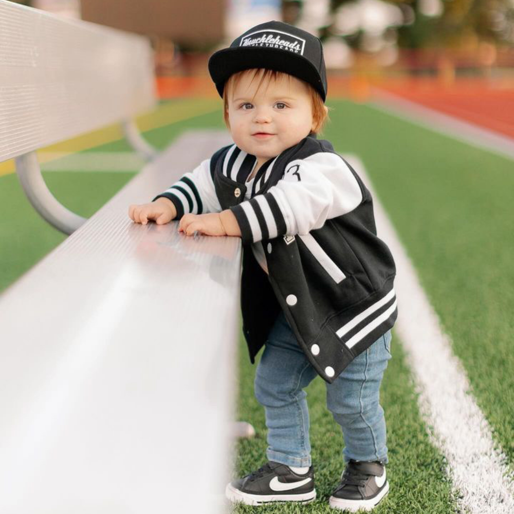 Model wearing a Black Kids Trucker Hat with Knuckleheads Patch. A trendy and versatile accessory designed for kids. In classic black, it showcases a striking Knuckleheads patch on the front. Elevate your child's style with this fashionable hat, perfect for adding a touch of character to their outfits. Crafted with care, this black kids trucker hat with the Knuckleheads patch is a must-have addition to their wardrobe, suitable for various occasions and everyday wear.