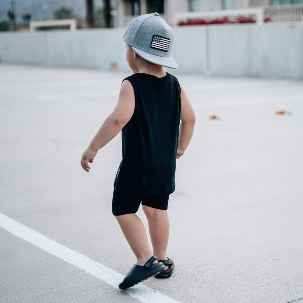 Model wearing a Grey USA Kids Trucker Hat with a black and white USA flag patch. A stylish and patriotic trucker hat designed for kids. The hat comes in a trendy grey color, featuring a striking black and white USA flag patch on the front. Elevate your child's style while proudly displaying their American spirit. Perfect for outdoor adventures and everyday wear, this hat is a fashionable and functional addition to their wardrobe.