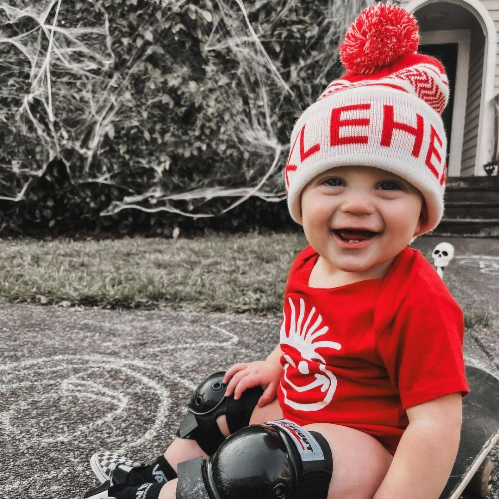 Image displaying a red and white fold-up beanie with a pom from Knuckleheads, designed for children. This versatile beanie combines a classic style with the Knuckleheads brand tag, perfect for infants and toddlers. A playful addition to the collection of Infant hats, enhancing its charm.