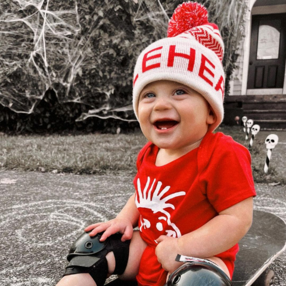 Image displaying a red and white fold-up beanie with a pom from Knuckleheads, designed for children. This versatile beanie combines a classic style with the Knuckleheads brand tag, perfect for infants and toddlers. A playful addition to the collection of Infant hats, enhancing its charm.