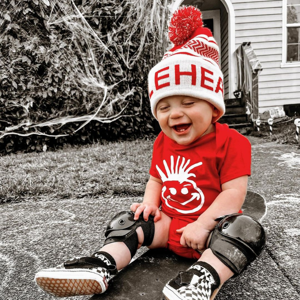 Image displaying a red and white fold-up beanie with a pom from Knuckleheads, designed for children. This versatile beanie combines a classic style with the Knuckleheads brand tag, perfect for infants and toddlers. A playful addition to the collection of Infant hats, enhancing its charm.