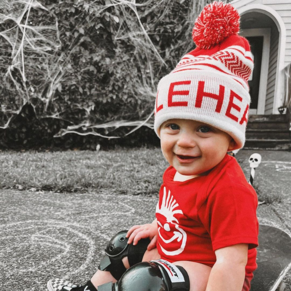 Image displaying a red and white fold-up beanie with a pom from Knuckleheads, designed for children. This versatile beanie combines a classic style with the Knuckleheads brand tag, perfect for infants and toddlers. A playful addition to the collection of Infant hats, enhancing its charm.